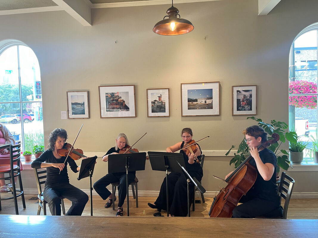 A string quartet plays a classical music work inside a small coffee shop.