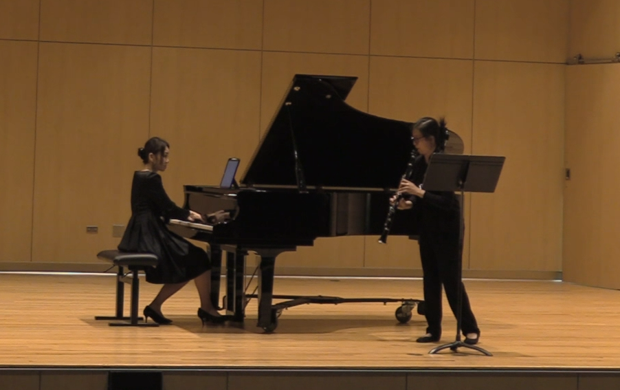 Eun-Hee Park (seated at a piano) and Irina Chang (playing clarinet) play the final notes of Distant Reflections work; they are on the stage of Hamre Recital Hall at Augustana University.