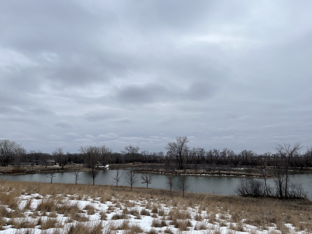 A view of a lake under a cloudy sky at Dakota Nature Park in Brookings, South Dakota. Some traces of snow are in the foreground.