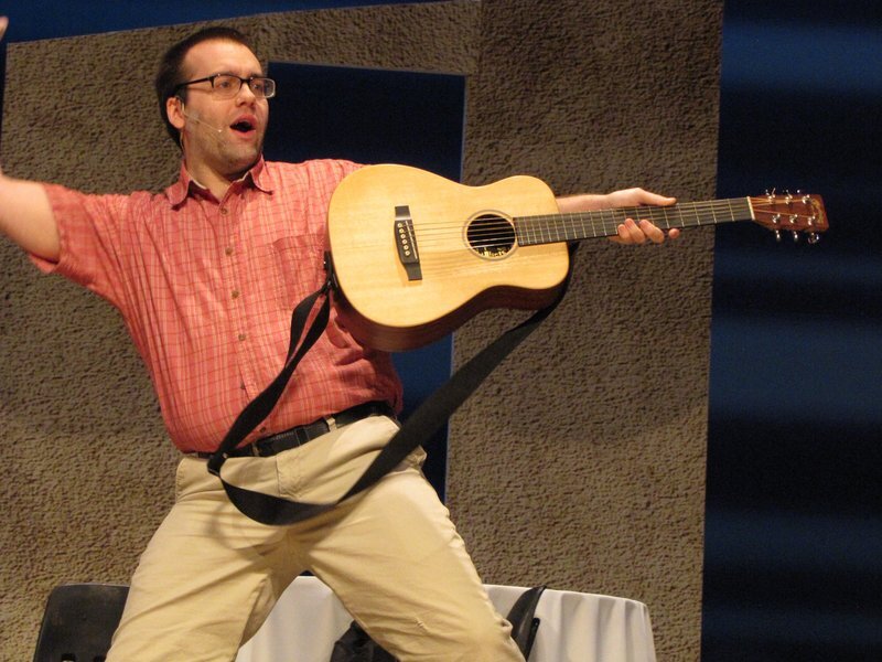 Connor Gibbs singing while holding an acoustic guitar.