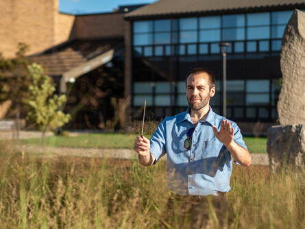 Connor poses with a baton, as if to be conducting an ensemble.