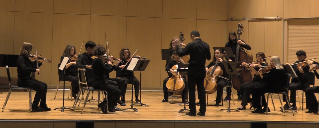 A string orchestra performs Connor's work on a recital hall's stage.