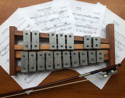 Piccolo glockenspiel posed with cello bow and sheet music of some of Connor's compositions.